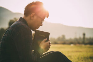 Man praying on the bible in sunny field alone