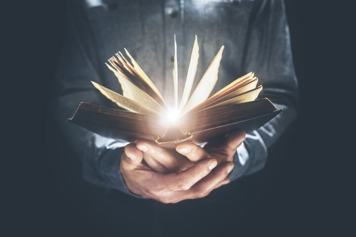 A person holding an open book, with light coming out of it, with both of their hands