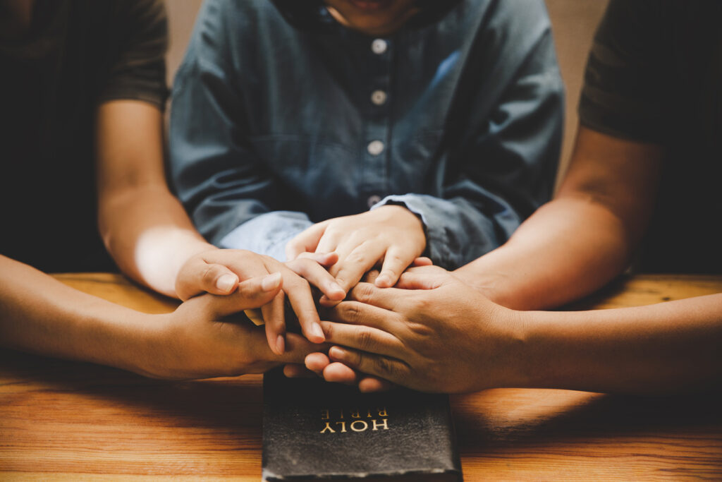 Life as a ministry coach - Family praying together with their hands on top of a bible.